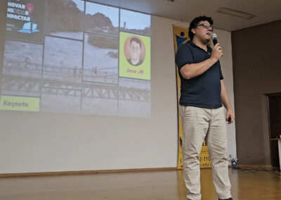 Jose JR vestindo camisa escura , calça bege segurando microfone no palco principal do Festival DevPira 2023 sendo Keynnote de encerramento.